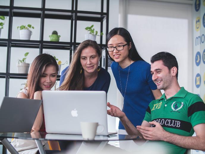 cuatro personas mirando un MacBook blanco sobre una mesa de cristal